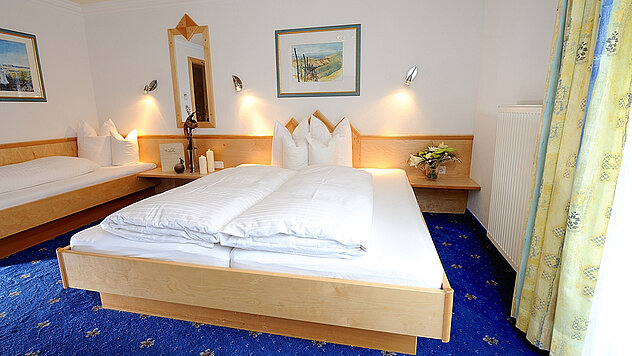 Mehrbettzimmer im Hotel Garni Valülla Ischgl mit Doppelbett, Einzelbett und blauem Teppich