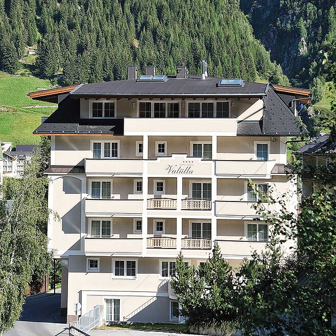 Modernes Alpenhotel mit Balkonen in sonniger Hanglage und Blick auf grüne Berglandschaft