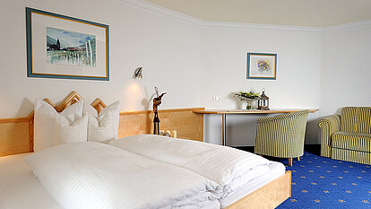 Doppelbett in einem Hotelzimmer mit blauen Teppichboden, Schreibtisch und zwei Sesseln