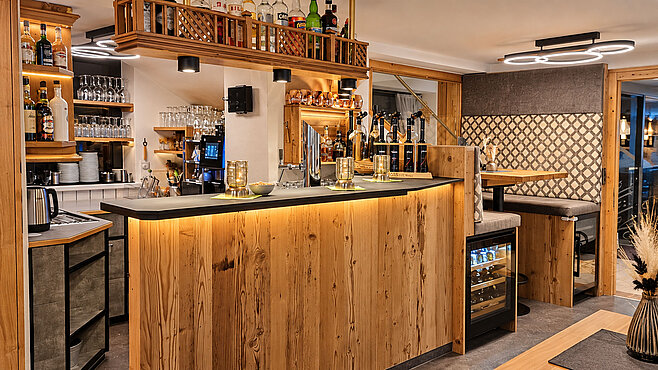 Gemütliche Hotelbar im Valuella mit rustikaler Holztheke, Spirituosenregal und gepolsterter Sitzecke.