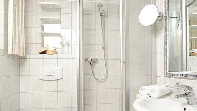 Helles Badezimmer mit Duschkabine, Waschbecken und Kosmetikspiegel im Hotel Garni Valülla Ischgl
