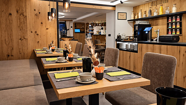 Frühstücksraum im Valuella mit gedeckten Holztischen, grauen Polsterstühlen und moderner Kaffee- und Teestation.