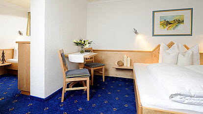 Hotelzimmer mit Doppelbett im Vordergrund und einem zusätzlichen Bett im Hintergrund, Tisch mit Stühlen