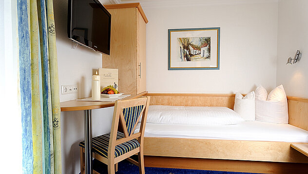 Einzelbett in einem Hotelzimmer mit Schreibtisch, Stuhl und Fernseher an der Wand