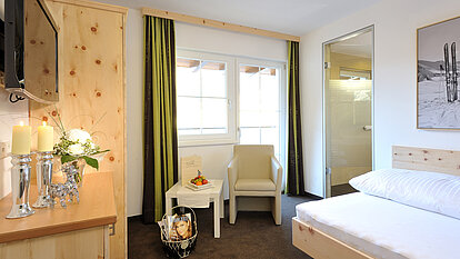 Hotelzimmer mit Bett, Sessel, Tisch mit Kerzen und großem Fenster mit Vorhängen