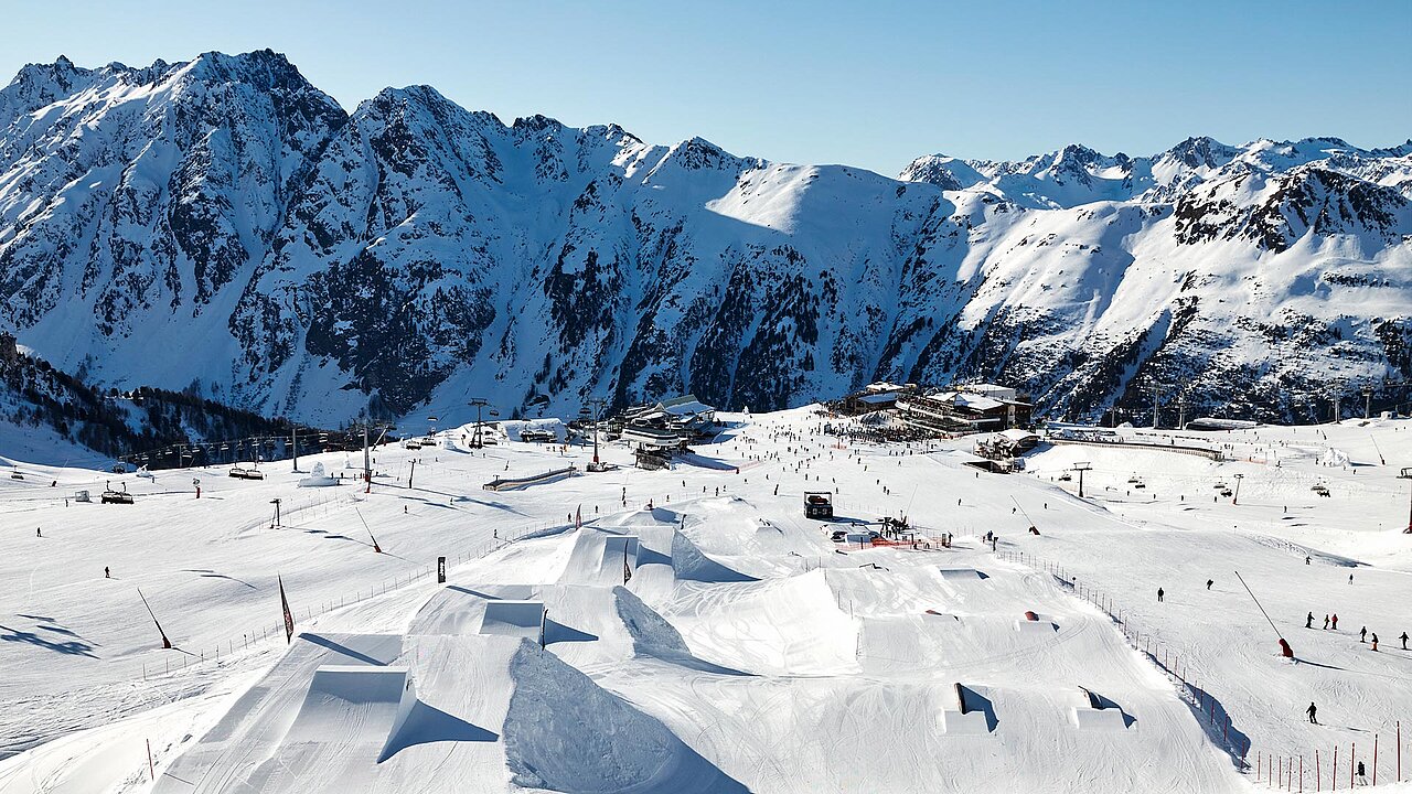Verschneites Skigebiet in Ischgl mit perfekt präparierten Pisten, zahlreichen Skifahrern und beeindruckender Alpenkulisse unter blauem Himmel.
