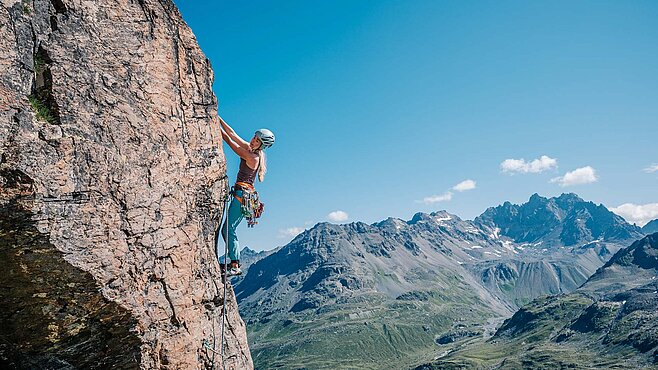 Kletterin in einer Felswand im Jamtal bei Ischgl, mit Blick auf beeindruckende Alpenberge und klare Sommerlandschaft.