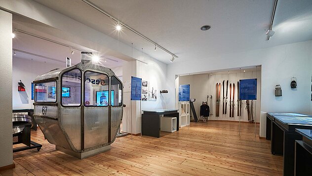 Innenaufnahme eines Museums mit historischen Ausstellungsstücken, moderner Beleuchtung und Holzfußboden.