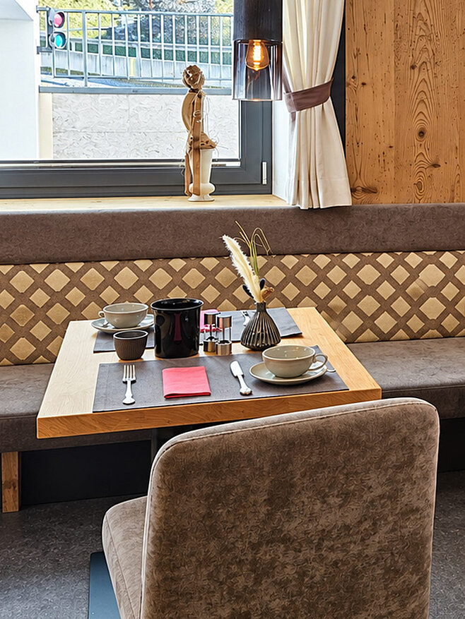 Gemütliche Frühstücksecke im Valuella mit zwei gedeckten Holztischen, gepolsterter Sitzbank und grauen Stühlen.