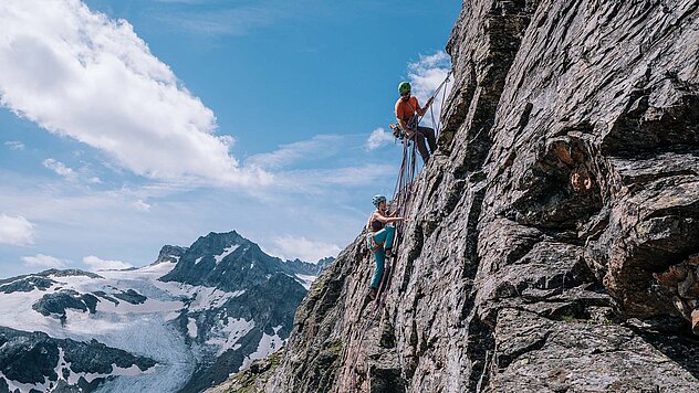 Zwei Kletterer in einer Mehrseillängenroute im Jamtal bei Ischgl, steile Felswand und Gletscherpanorama im Hintergrund.