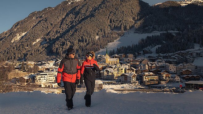 Paar beim Winterwandern oberhalb von Ischgl mit Blick auf das verschneite Dorf und die Kirche im Tal.