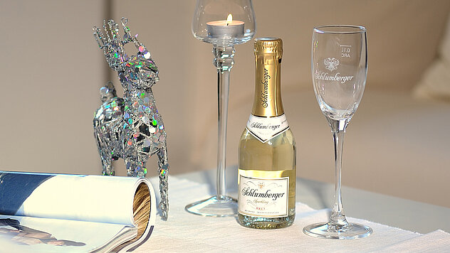 Flasche Sekt, Sektglas und Kerze auf einem Tisch, daneben eine silberne Rentier-Dekoration