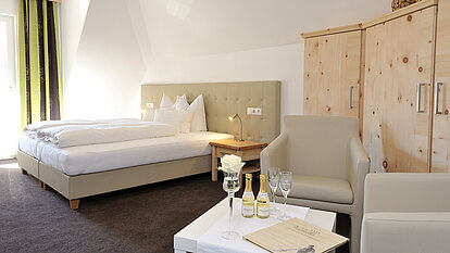 Hotelzimmer mit Doppelbett, Sofa, Fernseher und Blick auf ein Badezimmer durch eine Glastür