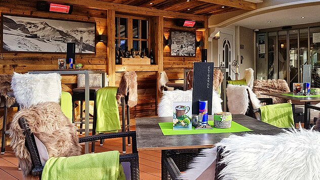 Gemütliche Sonnenterrasse in Ischgl mit Holzwänden, Lammfellen auf Stühlen und gedeckten Tischen – ideal für Après-Ski und Winterurlaub in Tirol.