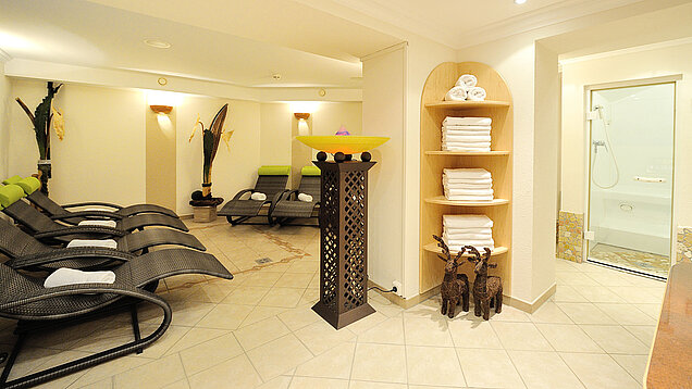 Wellnessbereich mit mehreren Liegen, Handtuchregal und Dusche im Hintergrund