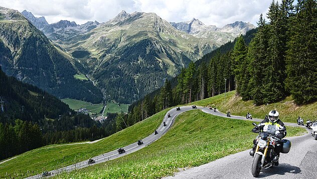 Mehrere Motorräder auf einer Bergstraße oberhalb von Ischgl mit Blick ins Paznauntal und grüne Alpenlandschaft.