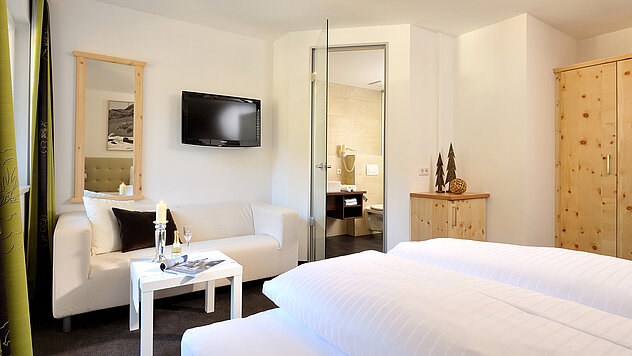 Hotelzimmer mit Doppelbett, zwei Sesseln, Tisch mit Sektflaschen und Kleiderschrank im Hintergrund